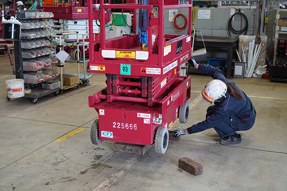 クレーンで吊った車体の下をのぞき込み、木片を置いていた従来の作業